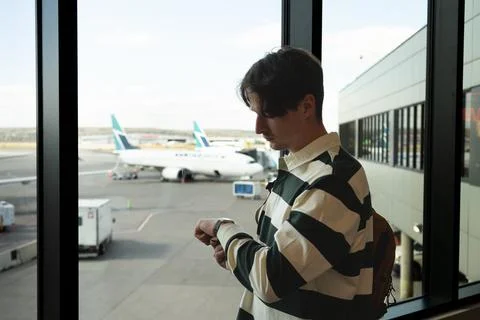 Man checks his watch while waiting at the airport, plane is in the background Stock Photos
