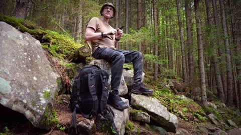 A man checks a knife while sitting on a stone. Video stock 311254524