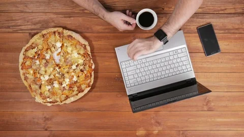A man checks the messages on a smart watch and eats pizza. He drinks coffee from Stock Footage