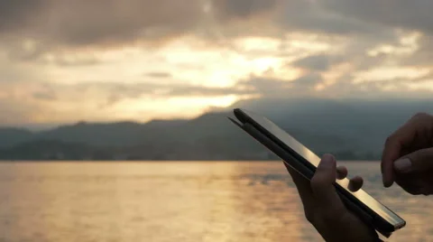 A man checks messages on the tablet during the sunrise on the beach of the ocean Stock Footage 67760194