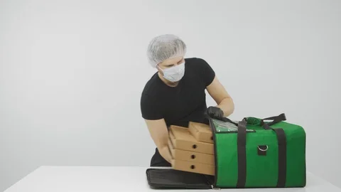 Man checks order on tablet and packs pizza in delivery bag 動画素材 129876575