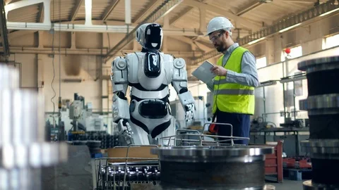 Man checks robot moving while typing on a tablet at a factory. Stock Footage