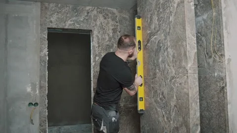 Man checks tile alignment in a bathroom renovation using a level tool Stock Footage 317380465