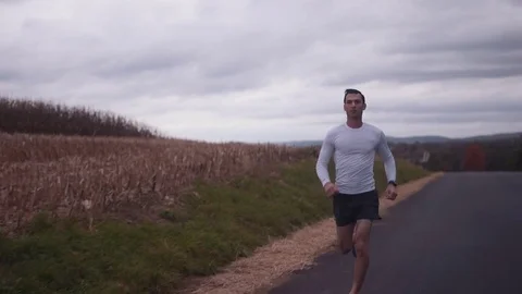 Man Checks Watch While Running Down Street Next to Field Stock Footage 81530066
