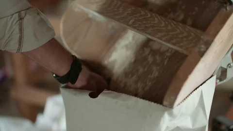 A man checks wheat grain that flows down into a bag inside a windmill Stock Footage 85214330