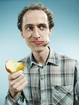 A man with a cheek bulging with a bite of apple, looking to the side Foto stock