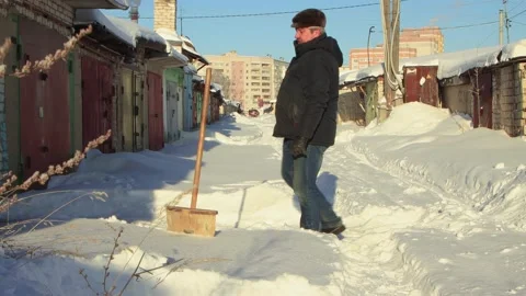 A man cheerfully clears the path to the garage from snow with a wooden shovel. Stock Footage 225416426