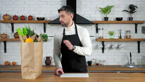 Man chef in black apron puts knife and board for cutting vegetables on kitchen Stock Footage 149469662