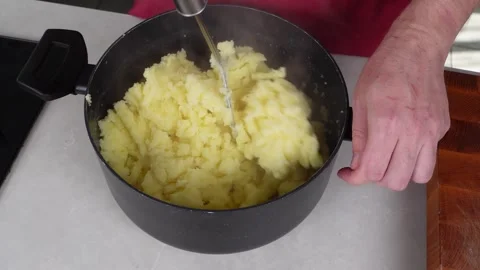 Man chef, donned in a red apron, skillfully mashes boiled potatoes in a pot Stock Footage 260233512