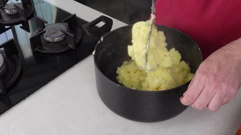 Man chef, donned in a red apron, skillfully mashes boiled potatoes in a pot Stock Footage 260233538