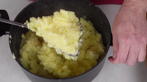Man chef, donned in a red apron, skillfully mashes boiled potatoes in a pot Stock Footage 260233557