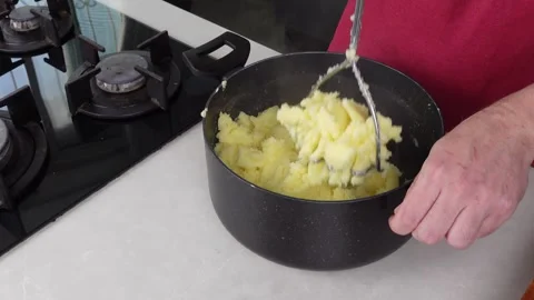 Man chef, donned in a red apron, skillfully mashes boiled potatoes in a pot Stock Footage 260234137
