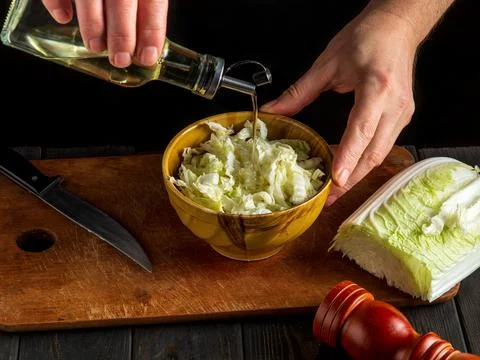 Man chef in uniform adding oil to napa cabbage salad. The idea of making Stock Photos