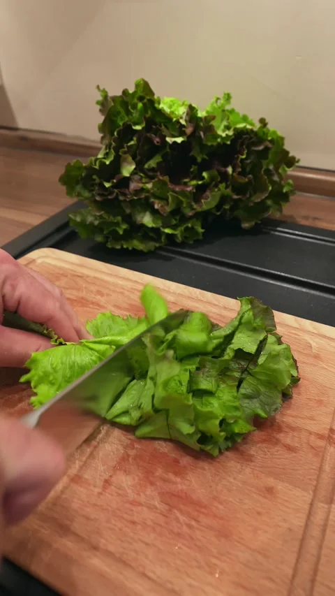 Man with chef's knife cutting fresh lettuce on wooden board in a kitchen Stock Footage 201265585