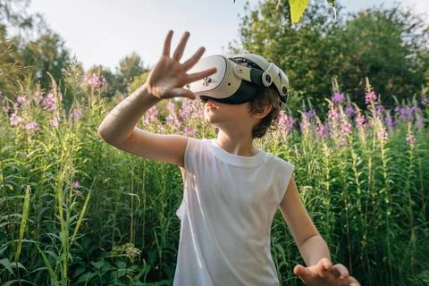 Man child boy in virtual reality glasses in flowers and grass plays Stock Photos