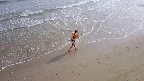 Man with child on his back runs on sea beach, endurance or fitness, aerial Stockbeeldmateriaal 109900575