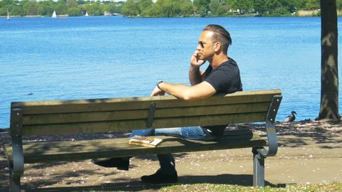 A man chills on the bench in fine weather and talks calmly on the mobile phone Stock Footage 89642467