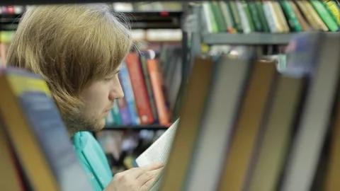 Man chooses a book in the library. He is in the corridor between the book series Stock Footage 85566100