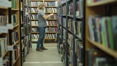 Man chooses a book in the library. He is in the corridor between the book series Stock Footage 85566129