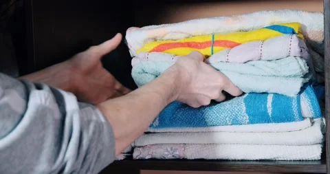 A man chooses a clean towel from a stack of clean towels on a shelf 库存影片 170667314