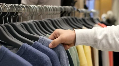 A man chooses colored sweaters on a hanger in clothing store. Stock Footage 165748234
