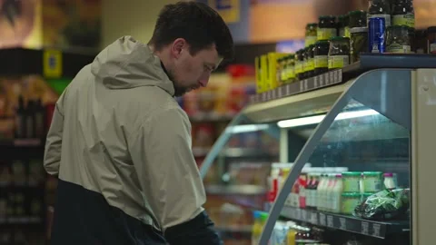 Man chooses salad while holding packet of milk in hand at supermarket in jacket Stock Footage 225140006