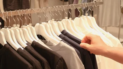 Man chooses white and black sweaters hanging on hanger in store. Stock Footage 340368490