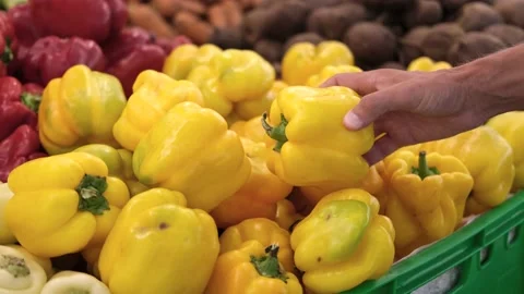 A man chooses a yellow pepper on a store counter. Stock Footage 211614771