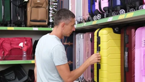 A man chooses a yellow suitcase in a store. Buying a suitcase for travel Stock Footage 237780129