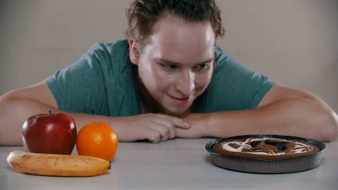 Man is choosing between cake and fruits on the table Stock Footage 118473559