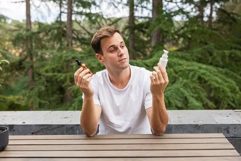 Man choosing between two cosmetic products for his skincare routine outdoors, Stock Photos