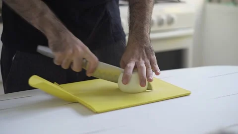 A man chopping onions with a sharp knife over a white table. Indoors, kitchen. Stock Footage 148053576