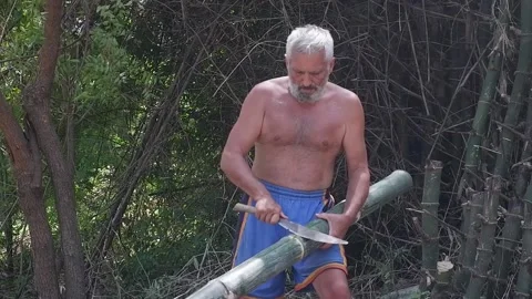 A man chops bamboo with a machete. They build a house. Video stock 158848655