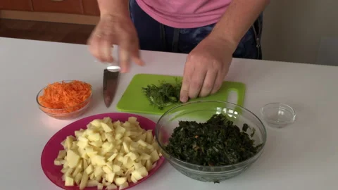 A man chops dill on a cutting board. Nearby are potatoes, carrots and sorrel. Stock Footage 136253570