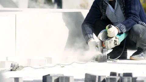 Man city worker cuts paving slab and puts near wall in city park Stock Footage 243660298