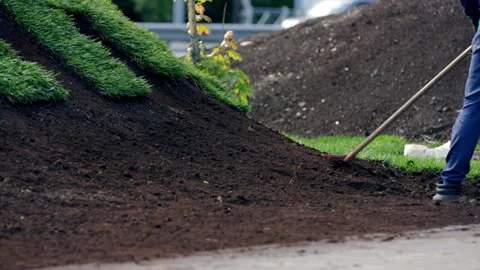 Man city worker levels black soil with rake in city park Stock Footage 243298938