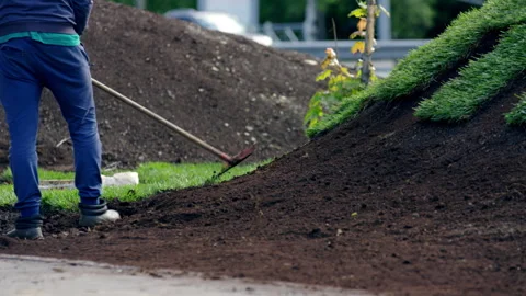 Man city worker levels black soil on hill in city park Stock Footage 244635236