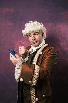 Man in classic renaissance clothes using an old monocle to see the mobile phone Stock Photos