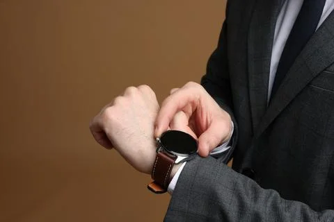 Man in classic suit checking time on brown background, closeup. Space for tex Stock Photos