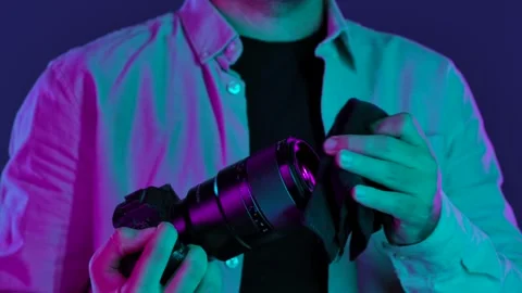 Man Cleaning Camera Lens with Cloth Under Purple Light Stock-Footage 334107580