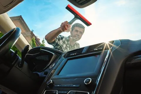 Man cleaning car windshield with squeegee from outside Stock Photos