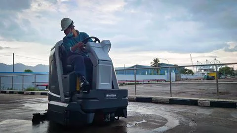 A man is cleaning a cement floor using a floor cleaning machine in a cement.. Stock Photos
