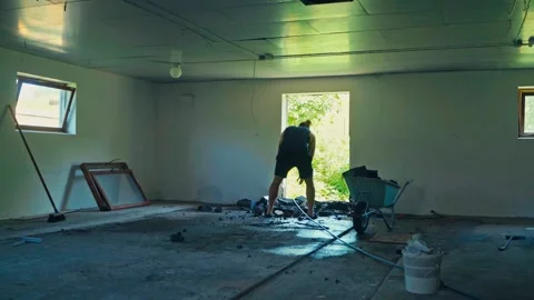 A Man is Cleaning Up Debris Inside a Room, Using a Wheelbarrow to Collect and Stock Footage 334351223
