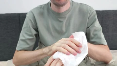 Man cleaning hands with a wet wipe while sitting on a couch. Hygiene routine Stock Footage 284045056