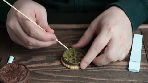 Man cleaning marijuana grinder from grinded cannabis with wooden chopstick. Stock Footage 128070760