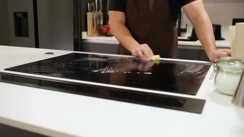 Man cleaning a modern induction cooktop with a sponge Stock Footage 345733081