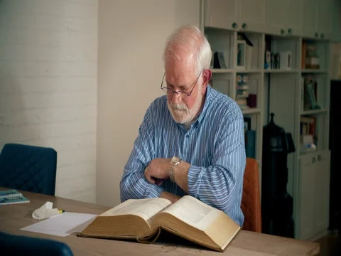 Man cleaning reading glasses and reading big historical  book Stock Footage 74398371