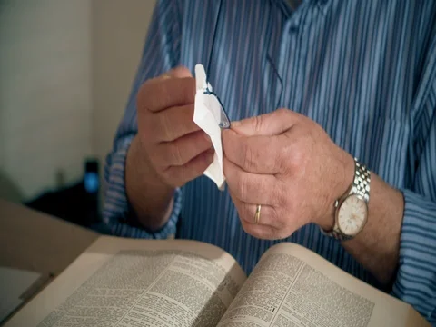 Man cleaning reading glasses and reading big book Stock Footage 74398451