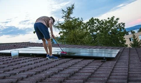 Man Cleaning Rooftop Solar Panels with Brush at Dusk Photos