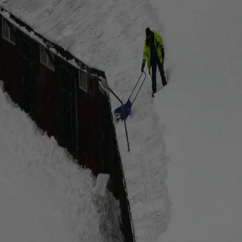 Man cleaning scraping snow off the rooftop using a special shovel Stock Footage 69557944